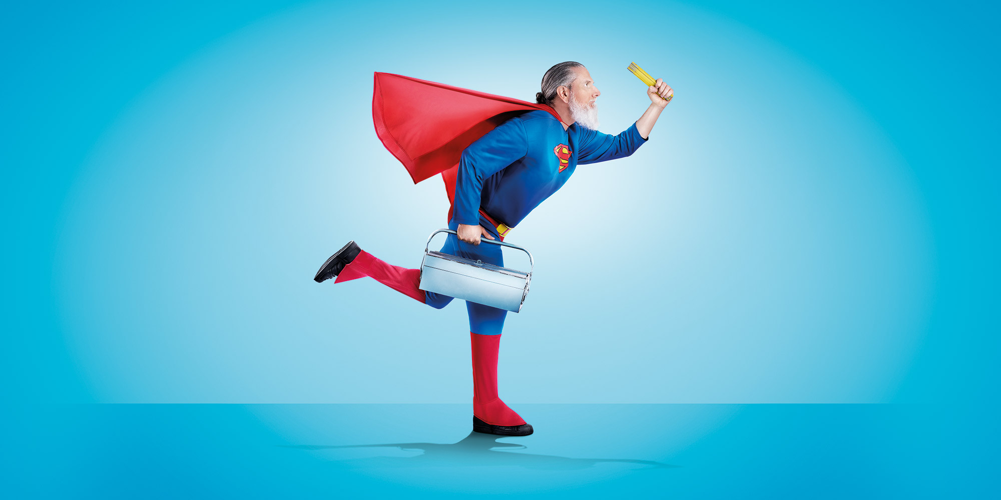 Bärtiger Mann im Superman-Kostüm mit Werkzeugkoffer im Laufschritt